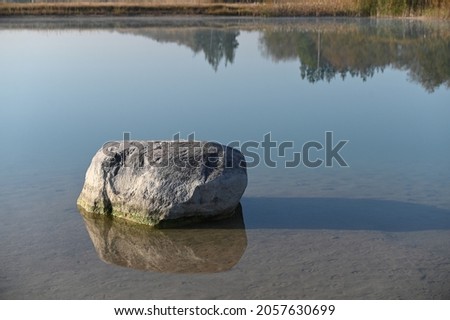 a large rock near the shore in the calm water of the lake