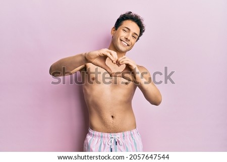 Young handsome man wearing swimwear shirtless smiling in love doing heart symbol shape with hands. romantic concept. 