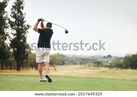A back view of a golfer after teeing off on a green golf course on a cloudy day