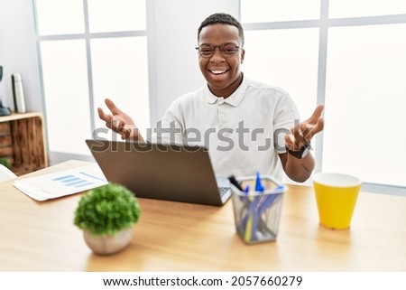 Young african man working at the office using computer laptop smiling cheerful offering hands giving assistance and acceptance. 