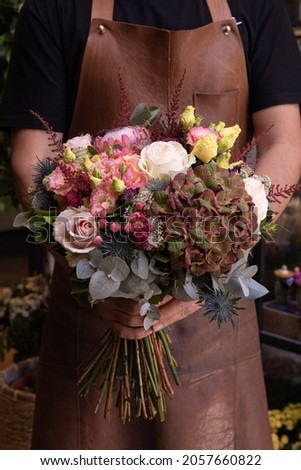 Beautiful autumn bouquet of pink and white roses, hydrangea macrophylla, king protea, eryngium amethystinum, eucalyptus branches and other plants at greek flowers shop in October. Vertical. Close-up.
