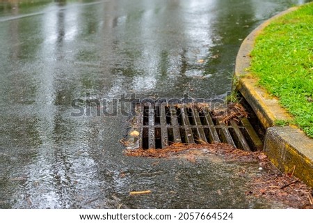 Metal storm drain during a rain event with leaves and needles starting to buildup around the edges Royalty-Free Stock Photo #2057664524