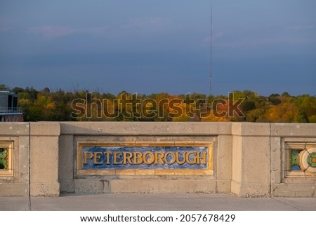 Sign Peterborough at the bridge wall, out of focus colorful fall forest in the background. Ontario, Canada.