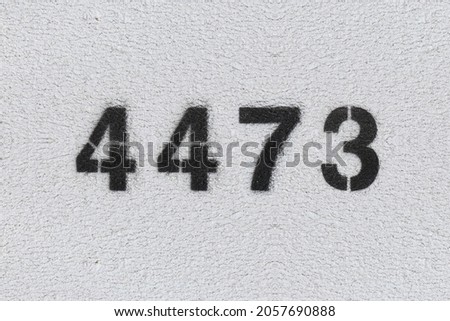 Black Number 4473 on the white wall. Spray paint. Number four thousand four hundred and seventy three.