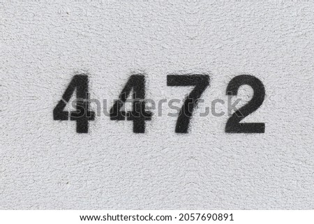 Black Number 4472 on the white wall. Spray paint. Number four thousand four hundred and seventy two.