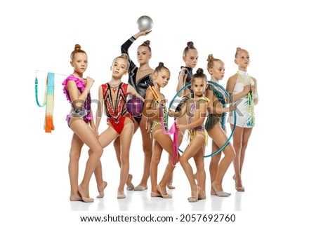 Little girls wearing colorful gymnastics attires with sport equipment. Studio shot of group of mixed-ages beautiful rhythmic gymnastics artists posing isolated on white studio background.