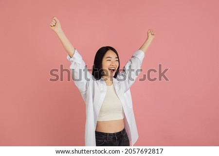 Happy winner, celebrating. Asian young woman's portrait on pink studio background. Beautiful female model in casual style. Concept of human emotions, facial expression, youth, sales, ad.