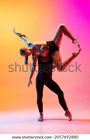 Two dancers, stylish sportive couple dancing contemporary dance on colorful gradient yellow pink background in neon light. Concept of art, creativity, movement, style and fashion, action.