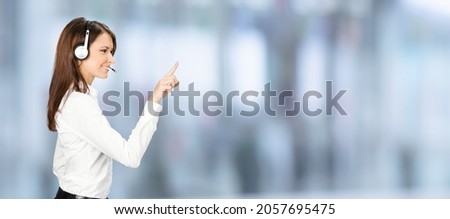 Call center service. Profile side image of customer support phone sale operator in white cloth, headset showing pointing clicking at copy space, imaginary text, standing over blurred office background