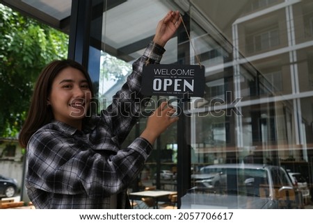 Photo of young restaurant owner while turning the sign over the restaurant glass as a background.