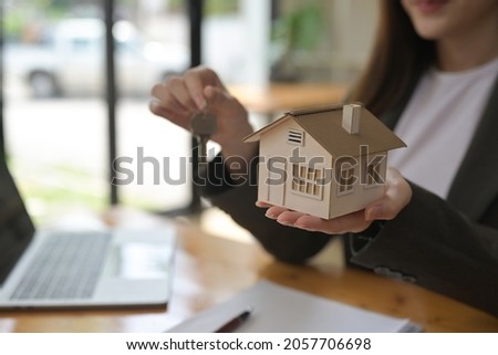 Photo of a businesswoman showing a house model and key while sitting at the wooden working desk. Broker and Dealer concept.