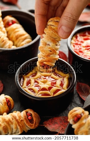 Mummy dogs dipped in ketchup and mustard sauce, close up view. Halloween funny food idea for party 