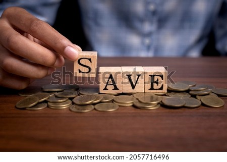 Woman hand holding wooden cube text "save" on pile of coins, money saving concept.
