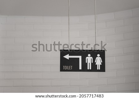 Toilet or Restroom with gender icon direction signboard which is hanged down from ceiling in gray tone. Sign and symbol object photo.