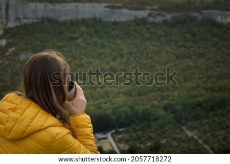 Young female traveler tea mountain. A girl is sitting on the top of a mountain with a beautiful autumn forest. The concept of traveling, enjoying nature, privacy, relaxation. Hot drink hands close up