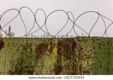 flat rusted sheet metal fence with peeled off green paint and barbed wire on top of it.