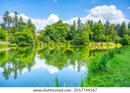 Summer in park. Green trees, blue sky and white clouds reflected in the water