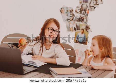 Smart little girl wearing eyeglasses, sitting at table, using notebook, studying at home. Back to school, distant online education concept.