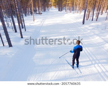 Man athlete trains cross-country skiing in winter on snow covered track in forest.