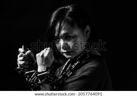 Powerful, aggressive, mature woman with fists up in the air, fights back against the symbolic chains wrapped around her neck and wrists. Black and white image. Royalty-Free Stock Photo #2057764091