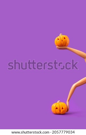 Pumpkins in the hands of a plastic doll on a pastel purple background. Minimalistic Halloween concept. Creative idea.