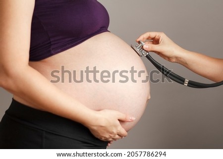 An isolated shot of a pregnant woman being examined by a doctorpregnant woman being examined by doctor on gray studio background, stethoscope on belly,healthy family planning concept
