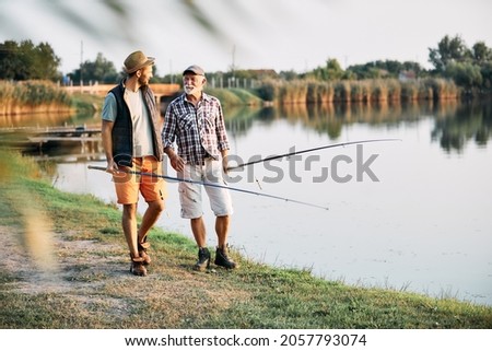 Smiling mature man and his adult son communicating while fishing in freshwater. Copy space. Royalty-Free Stock Photo #2057793074