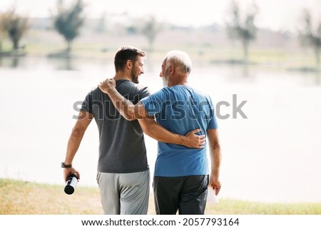 Back view of happy athletic man and his senior father walking embraced while exercising in nature. Copy space. Royalty-Free Stock Photo #2057793164