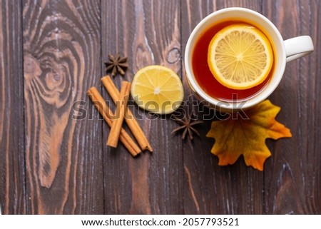 A cup of tea with lemon and cinnamon sticks on a wooden table, warm knitted snood. autumn mood