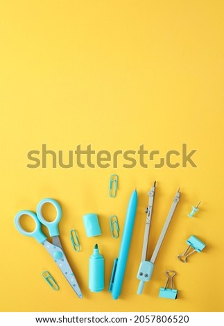 Blue stationery items on the yellow background with free space for text. Creative, colorful background with school supplies. Flatlay with copy space, top view. Marker, pen, paper clips, scissors.