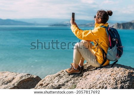 A traveler takes a selfie on her phone against the background of the sea, Close-up. Travel and active lifestyle concept. A woman holds a phone in her hands against the background of the blue sea.