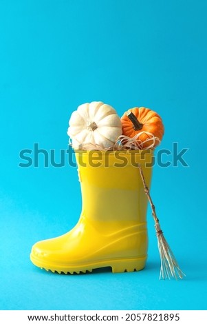 Yellow autumn boot with two pumpkins white and orange and witch broom. Minimal halloween idea on blue background.