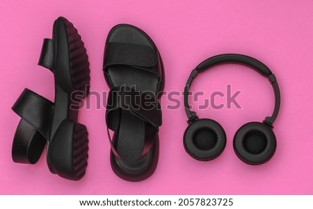 Black leather sandals and stereo headphones on pink background. Top view