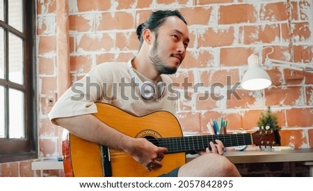Artists producing music in their home sound studio, Asian man playing guitar and singing in living room at home. Lifestyle man relax in morning at home concept. Royalty-Free Stock Photo #2057842895