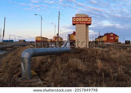 The village of Tavayvaam in the Far North of Russia in the Arctic. View of the pipeline, houses and a roadside sign with Russian text "State farm named after the XXII Congress of the CPSU". Chukotka.