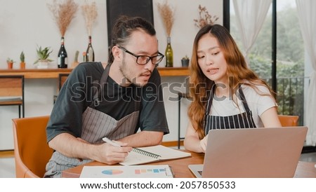 Stressed Asian small business owners couple using laptop discussing project and finance with documents of shop for the month at cafe. Woman and man doing paperwork together, paying taxes online. Royalty-Free Stock Photo #2057850533