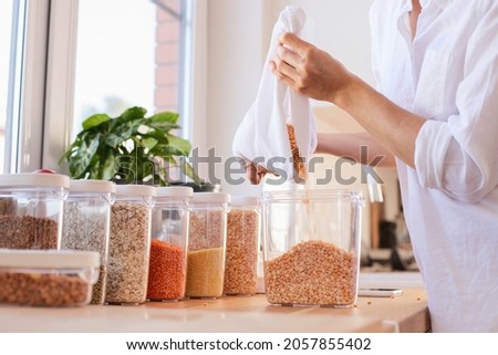 Organization in the kitchen. The girl pours cereals, legumes into containers. Zero waste, eco friendly concept. Royalty-Free Stock Photo #2057855402