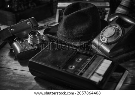 Old vintage cinematic noir scene, detective's desk with a hat, telephone, camera, portable cassette recorder, and whisky Royalty-Free Stock Photo #2057864408