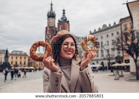 Tourist woman eating bagel obwarzanek traditional polish cuisine snack waling on Market square in Krakow. Traveling Europe in autumn Royalty-Free Stock Photo #2057885801