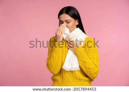 Virus outbreak, flu epidemic. Sick woman wrapped in scarf sneezing in napkin, cleaning running nose and coughing, suffering influenza symptoms, fever. `indoor studio shot isolated on pink background  Royalty-Free Stock Photo #2057894453