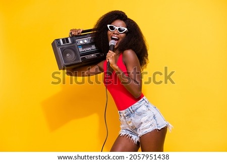 Photo of optimistic nice brunette lady hold boom box sing wear eyewear top shorts isolated on yellow color background