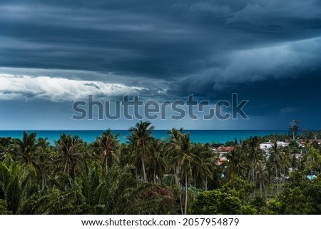Dramatic storm clouds over the sea, forest and rooftops on a summer day