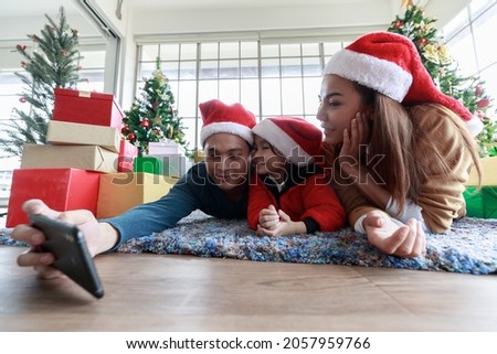 Asian Selfie holding smartphone Taking picture. Happy young family with kids fun celebrating Christmas. Christmas time. My dad, mom, and daughter in Santa hats lie about In front Gift box at home