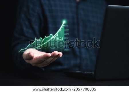 Trader holding green graph chart with arrow and using laptop computer for analysis stock market information , Investment concept.