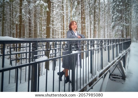 Portrait of a middle-aged woman in a forest or park with snow-covered trees. Model posing during photo shoot in cold time with snow