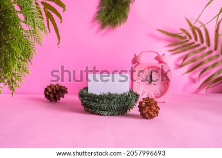 concept ideas that showcase the product. business card on pink background decorated with , dry leaves, pine leaves and clock. christmas composition
