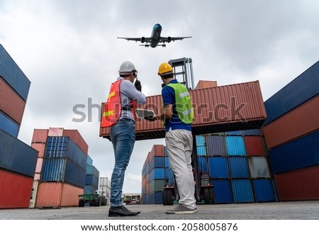 Industrial worker works with co-worker at overseas shipping container port . Logistics supply chain management and international goods export concept . Royalty-Free Stock Photo #2058005876
