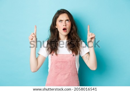 Shocked insulted young woman frowning, gasping and looking with disappointed and offended face, showing something disrespectful, standing against blue background