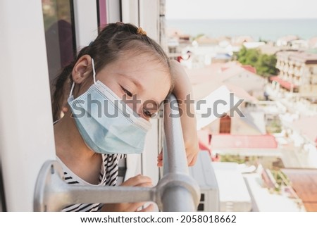 A little girl fell ill on vacation. The girl misses home because of the disease. Children in a medical mask. A girl looks out the window as other children walk.