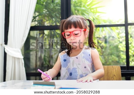 cute little asian girl Wearing red glasses, standing on the table at home drawing drawings. educational concepts, develop children's learning